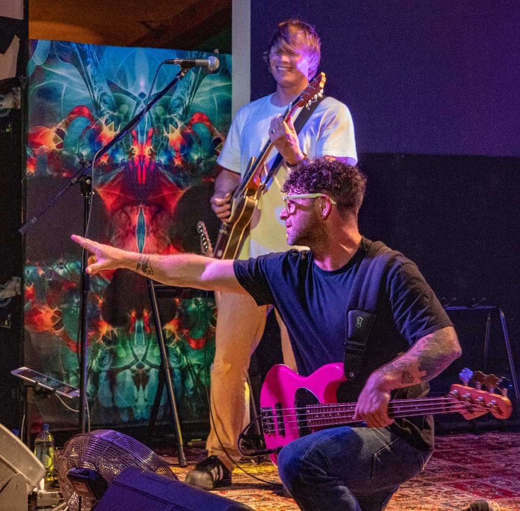 Musician kneeling on stage playing a pink bass guitar