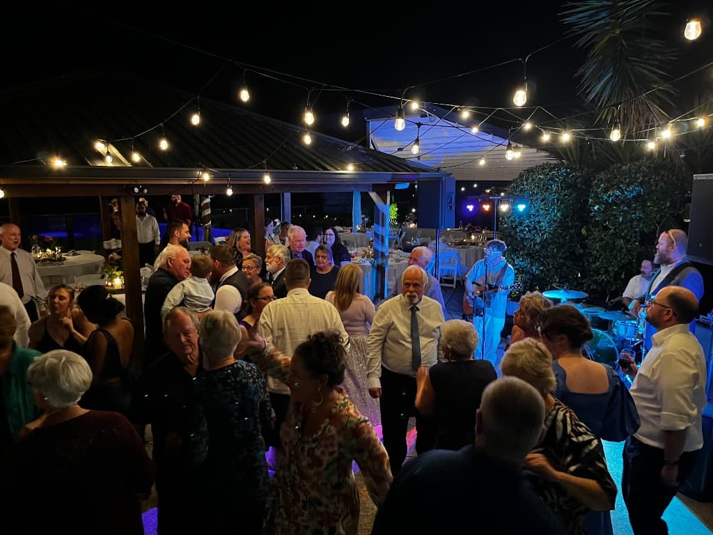 Joe Mac Band performing at outdoor wedding reception under string lights, crowd dancing